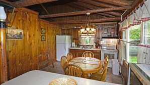 A rustic wooden interior with a dining table, chairs, a refrigerator, a stove, and a kitchen area with wooden cabinets and a hanging light fixture. - Countryside Cottages (Bartonsville)