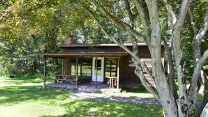 A rustic cabin with a porch, surrounded by lush greenery. - Countryside Cottages (Bartonsville)