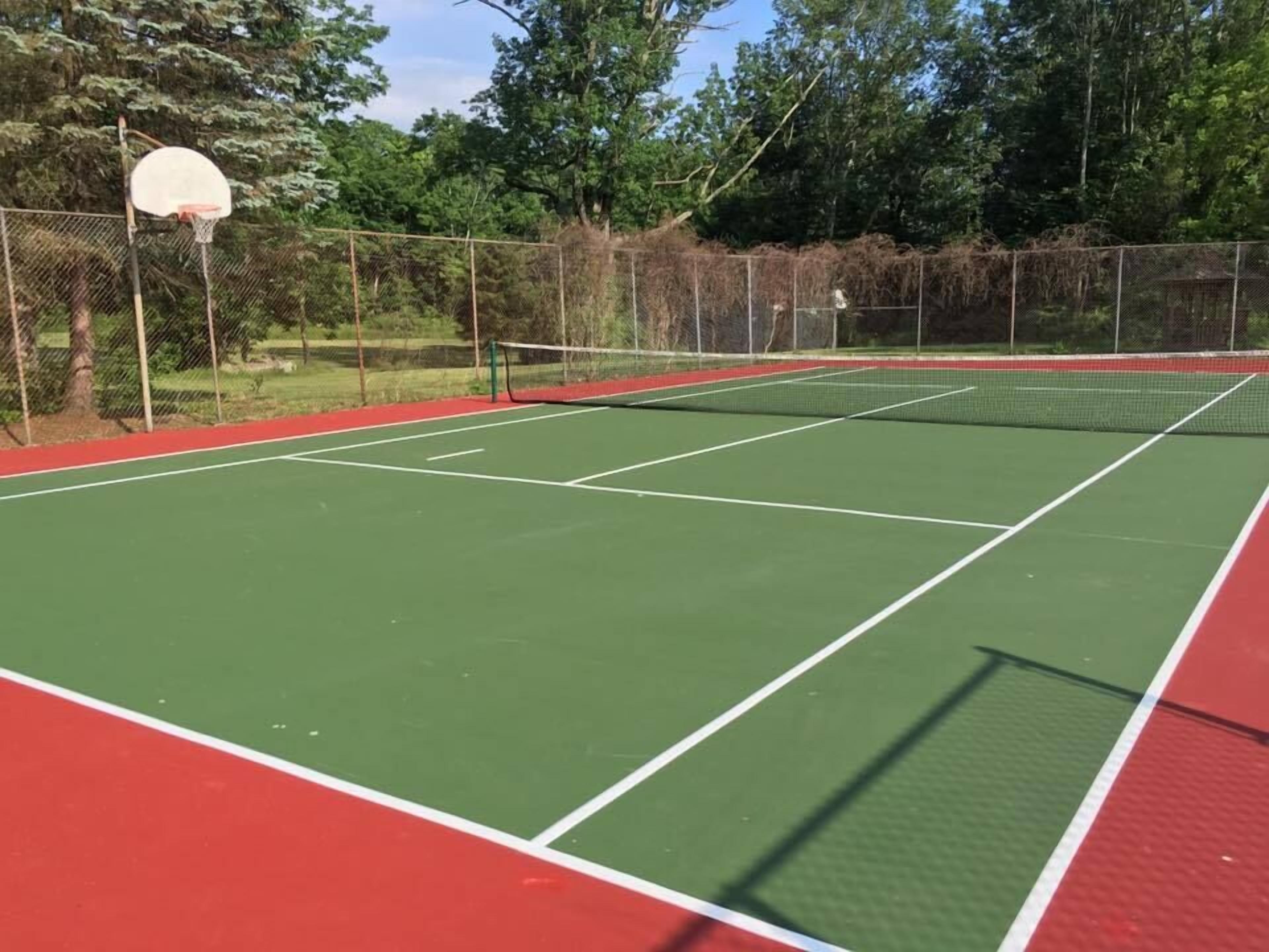 An outdoor tennis court with a net, surrounded by a fence and trees.