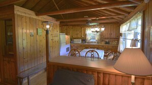 A wooden cabin interior with a dining area, kitchen, and a bench. - Countryside Cottages (Bartonsville)