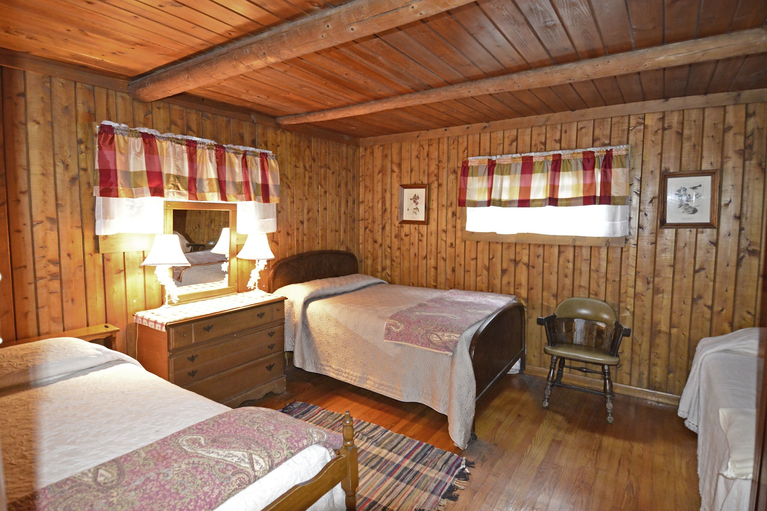 A wooden-paneled room with two beds, a chair, a dresser, and a mirror.