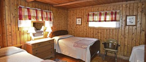 Una habitación con paneles de madera, dos camas, una silla, un aparador y un espejo.