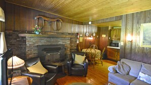 A cozy living room with a fireplace, leather furniture, and wooden walls. - Countryside Cottages (Bartonsville)