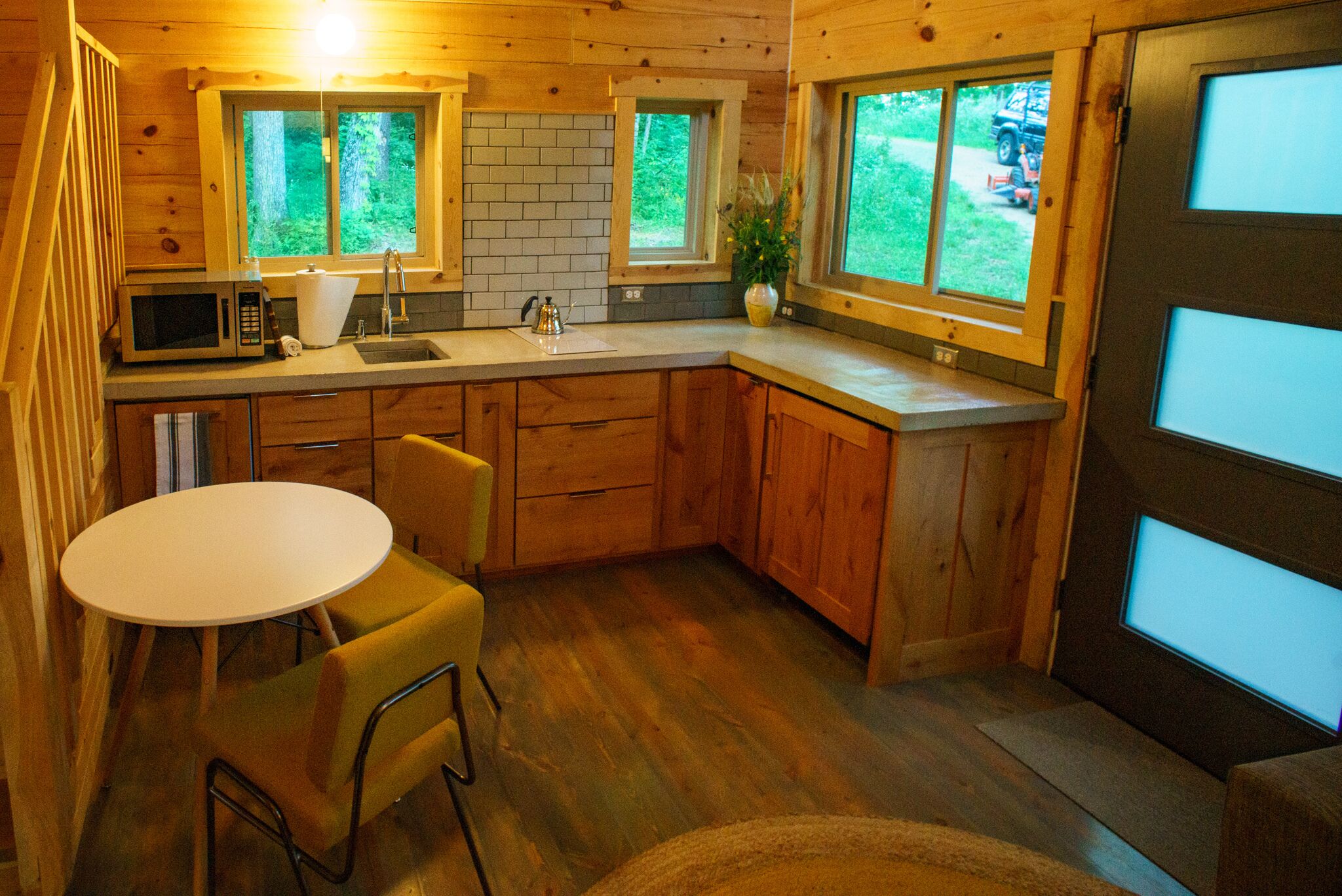 Une cuisine compacte avec des meubles en bois, un plan de travail blanc, un four à micro-ondes, un évier et une petite table à manger avec des chaises.