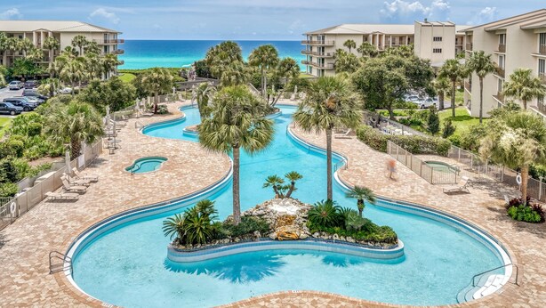 Un resort con piscina central, palmeras y vista al océano.