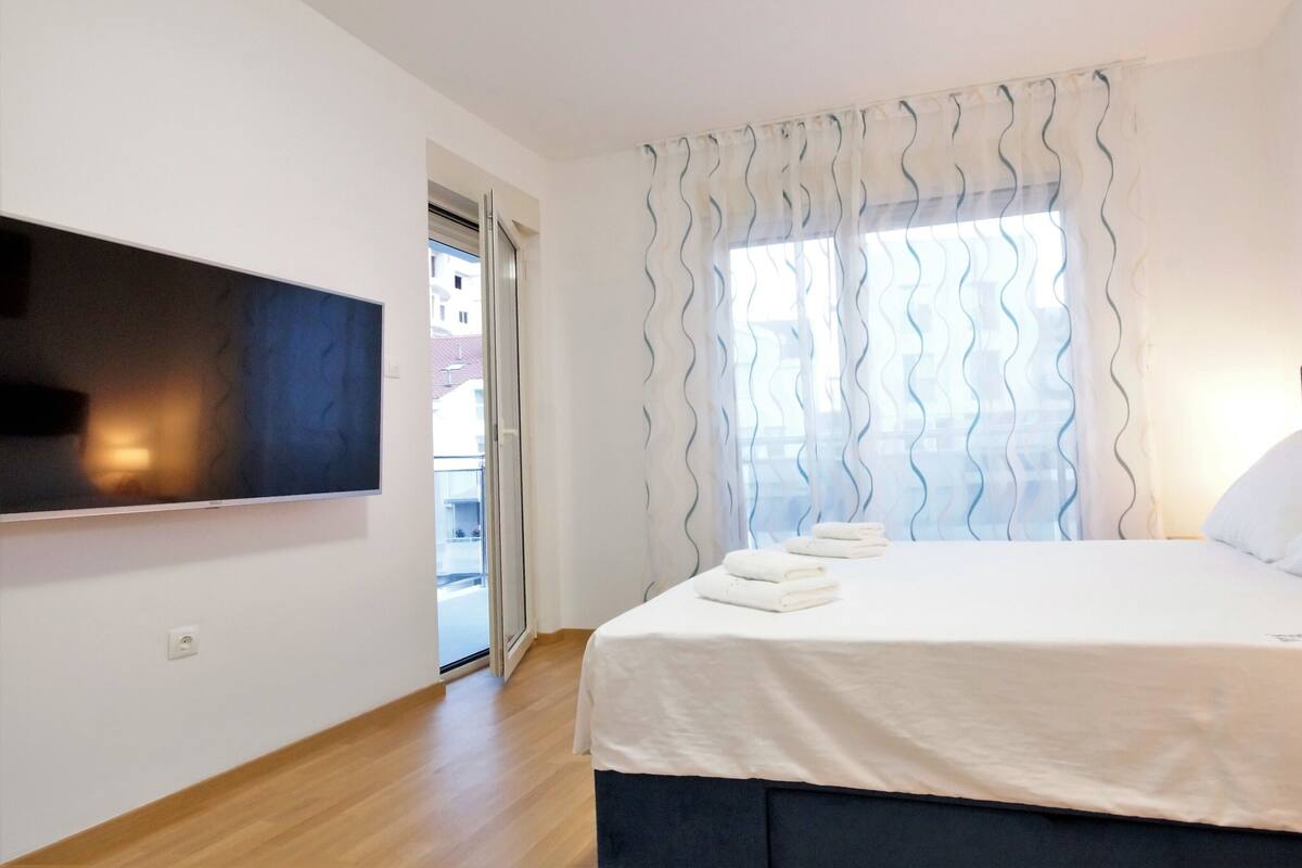 Un dormitorio con cama, televisión montada en la pared y ventana con cortinas.