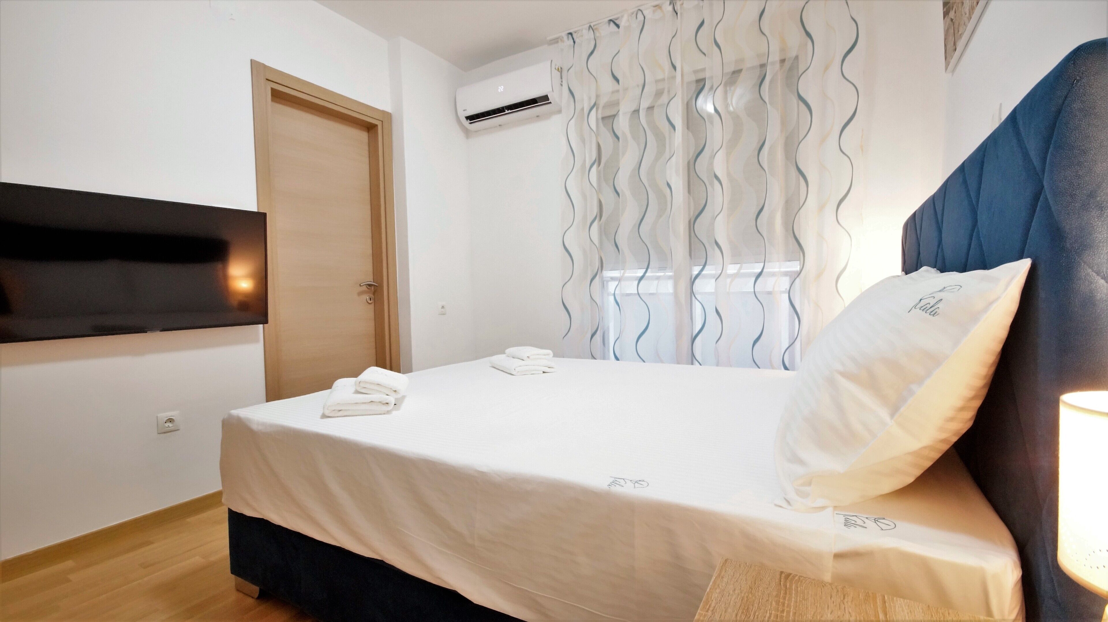 A hotel room with a bed, a TV mounted on the wall, an air conditioning unit, and a window with curtains.