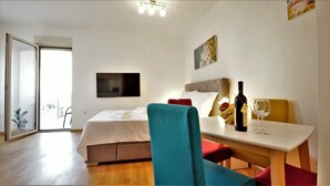 Habitación de hotel con cama, escritorio con botella de vino y copa, silla y televisor montado en la pared.