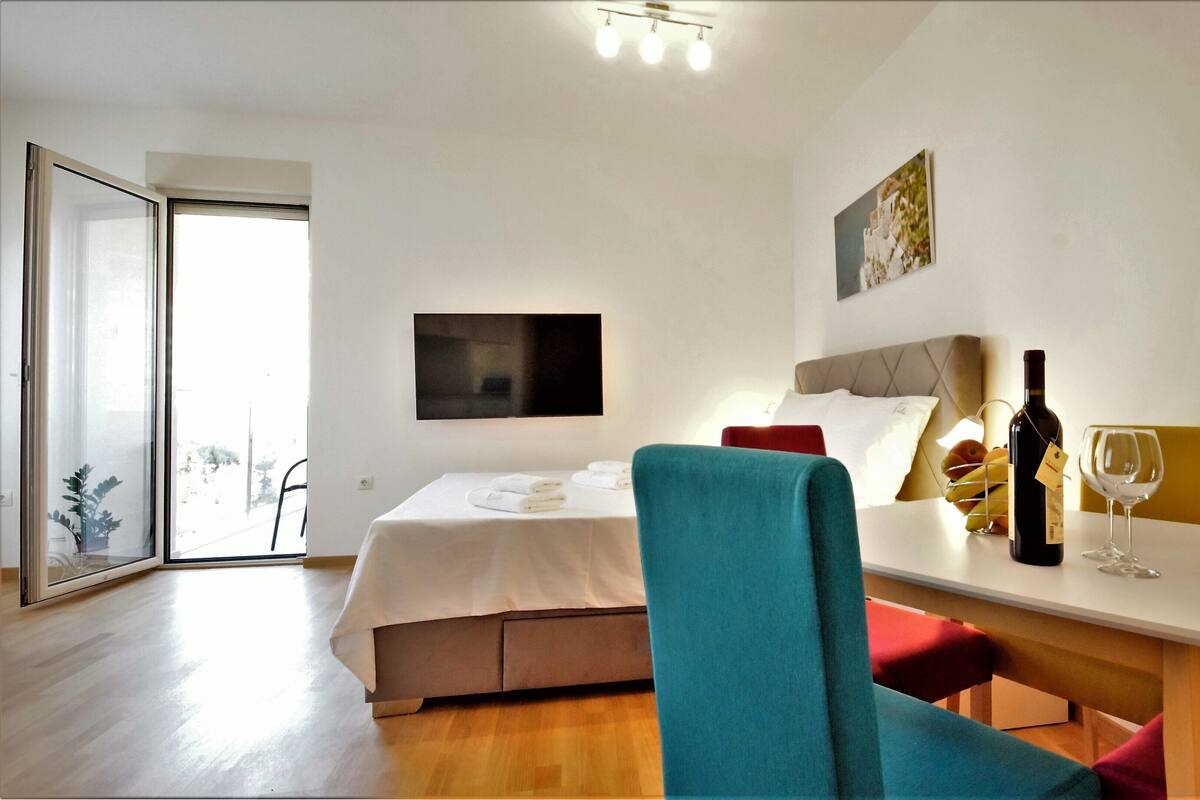 Habitación de hotel con cama, escritorio con botella de vino y copa, silla y televisor montado en la pared.