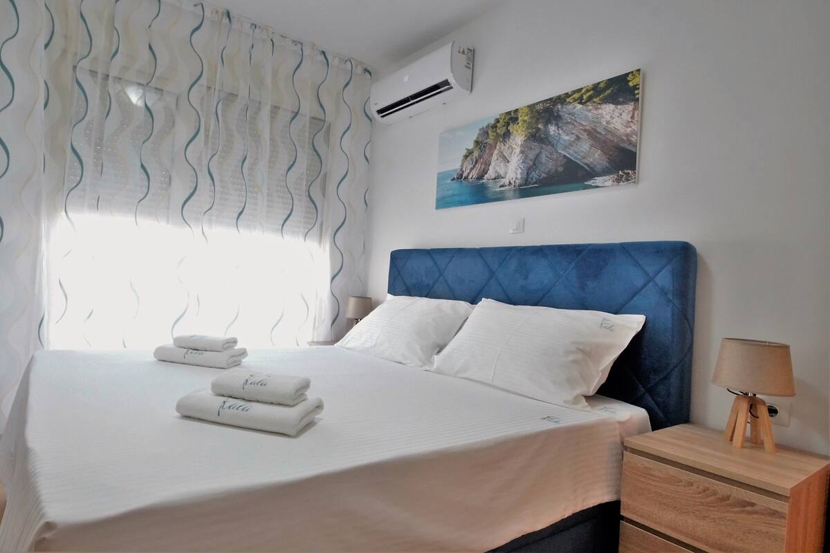 Habitación de hotel con cama, mesita de noche, lámpara, un cuadro y un equipo de aire acondicionado.