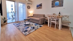 Una sala de estar con un sofá, una mesita redonda, una mesa de comedor con sillas, una araña y vistas al balcón exterior.