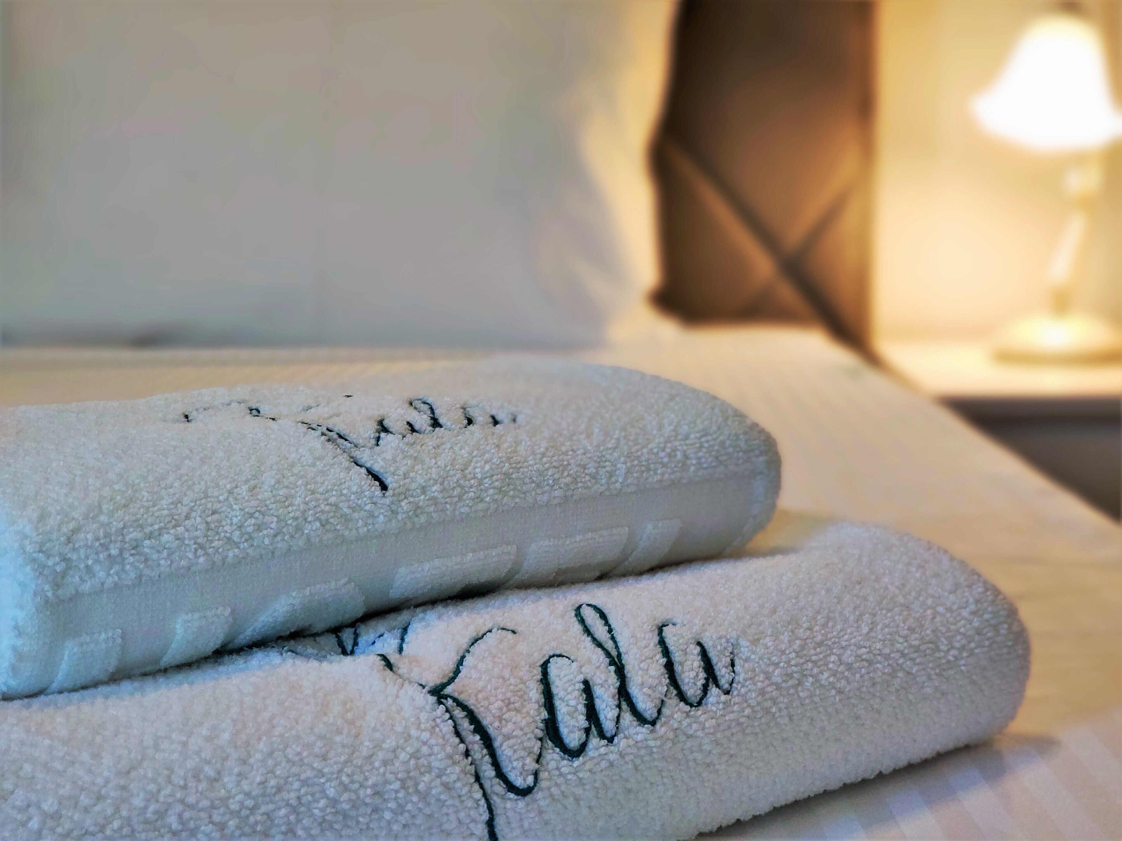 Two neatly folded towels with embroidered text on a bed.