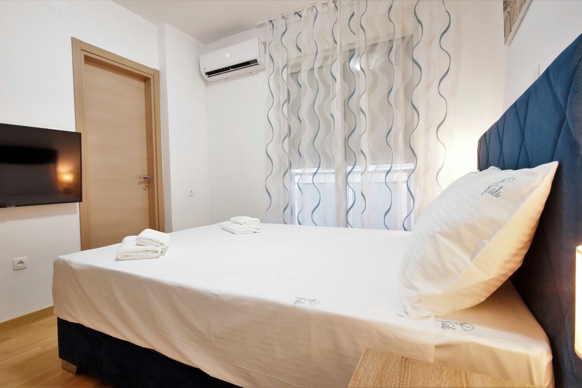 Una habitación de hotel con cama, televisor montado en la pared, aire acondicionado y ventana con cortinas.