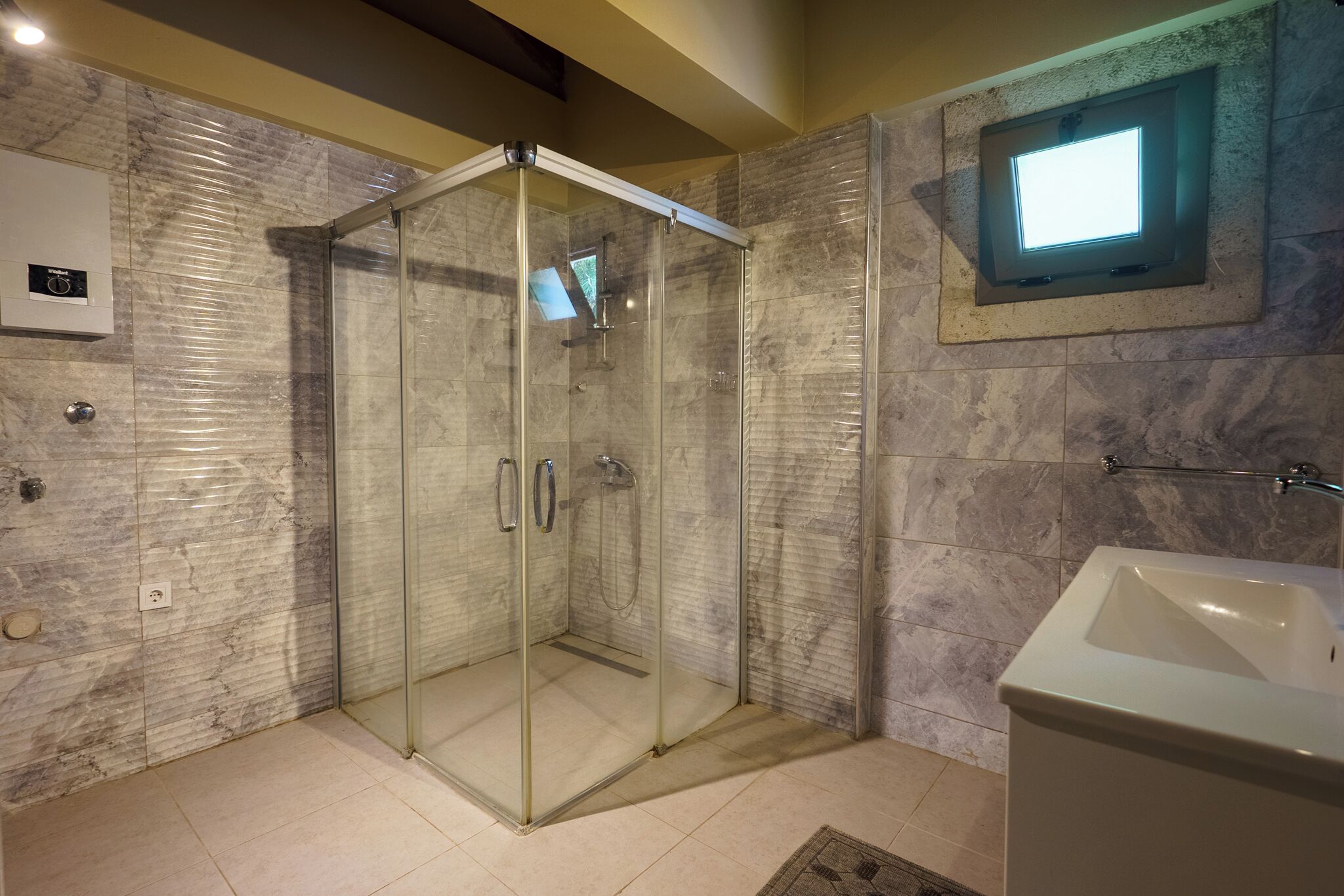 A modern bathroom with a glass-enclosed shower, a built-in sink, and a small window for natural light.