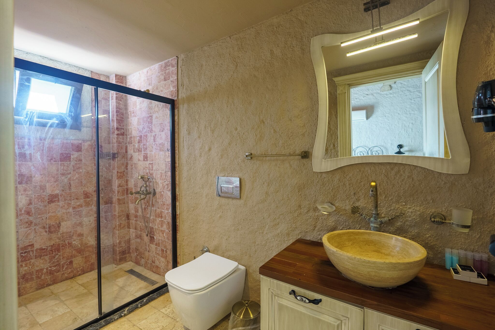 A bathroom with a glass-enclosed shower, a wooden vanity with a large bowl sink, and a wall-mounted mirror.