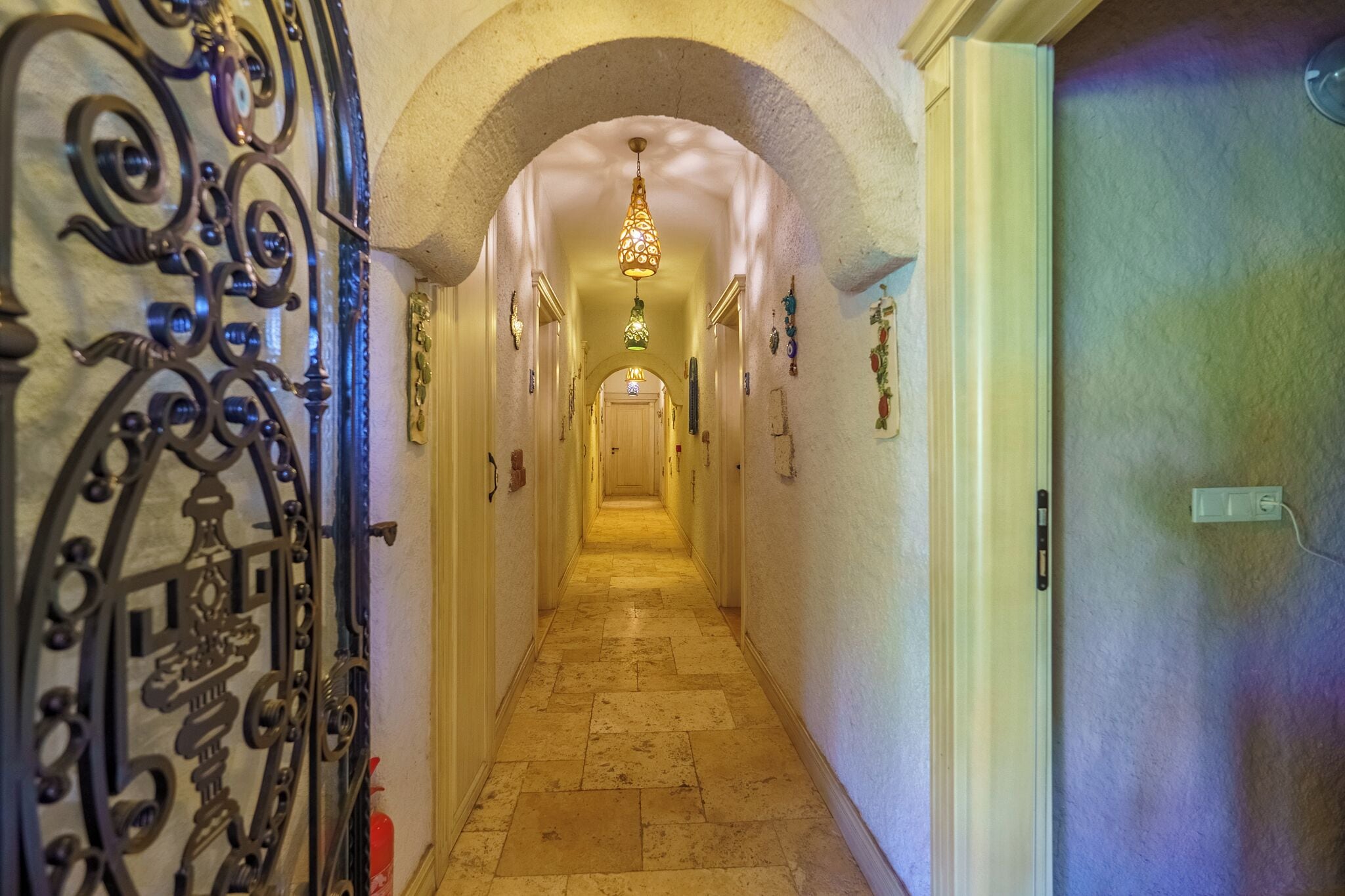 A hallway with an ornate metal gate, a tiled floor, and a chandelier.