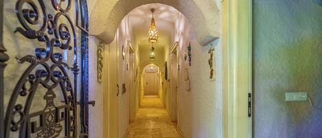 A hallway with an ornate metal gate, a tiled floor, and a chandelier.
