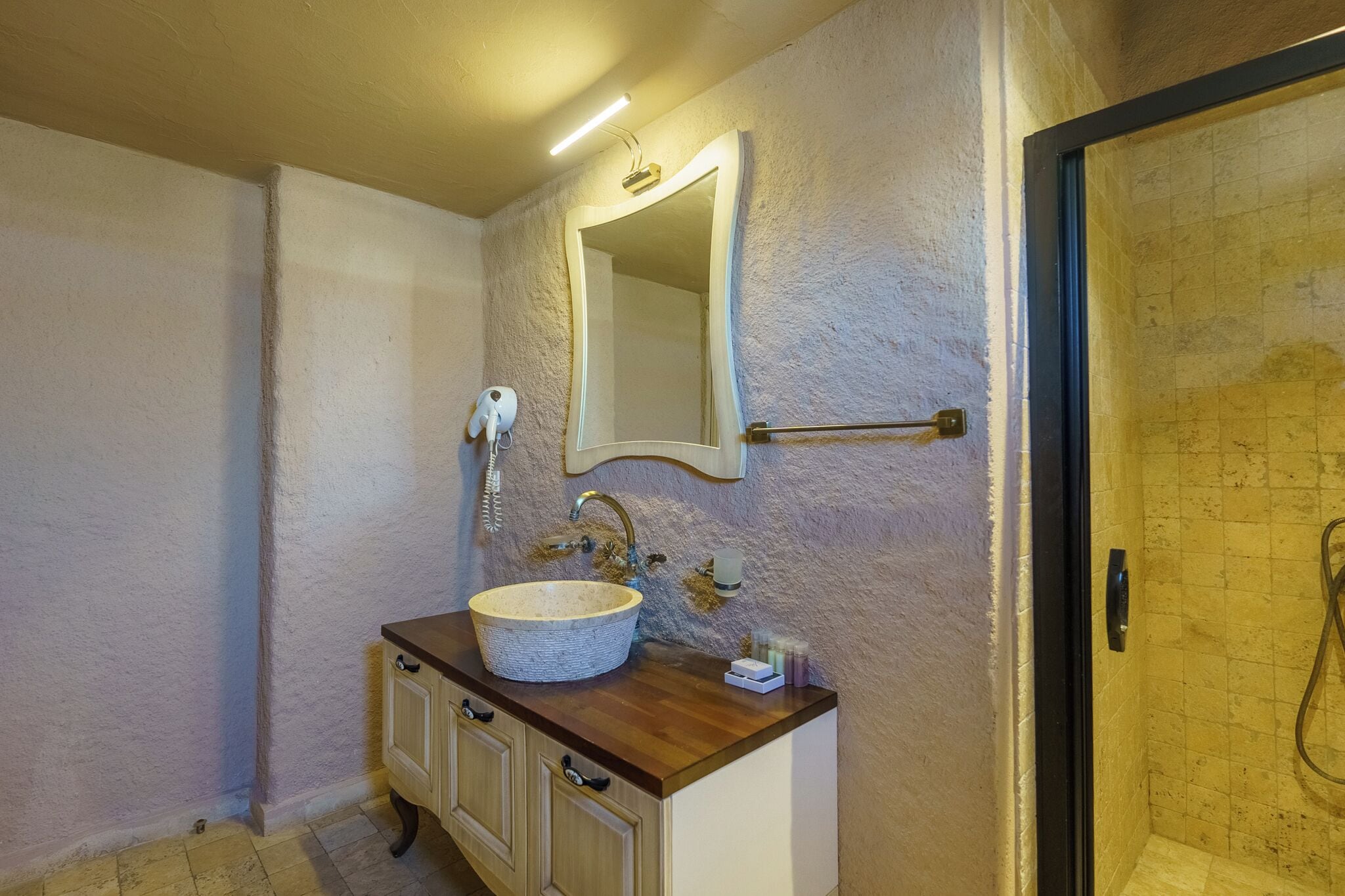 A bathroom with a stone sink, a mirror, a towel rack, and a shower area.