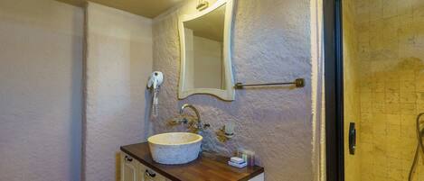 A bathroom with a stone sink, a mirror, a towel rack, and a shower area.