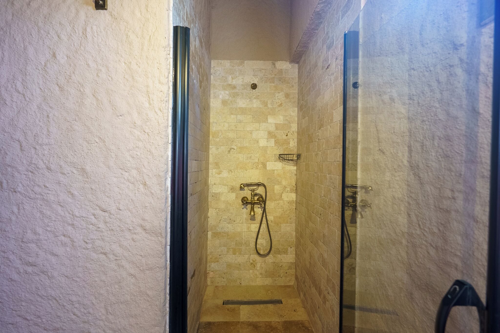 Un área de ducha estrecha y con azulejos, con puerta de vidrio, un cabezal de ducha y una alcachofa de mano.