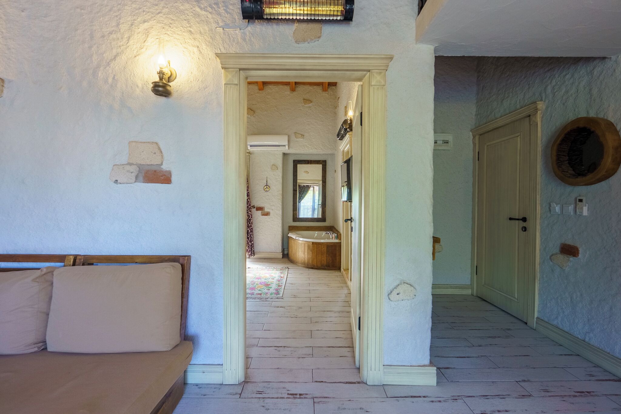 A room with a bed, a wooden door, a bathroom with a bathtub, and a hallway leading to another room.