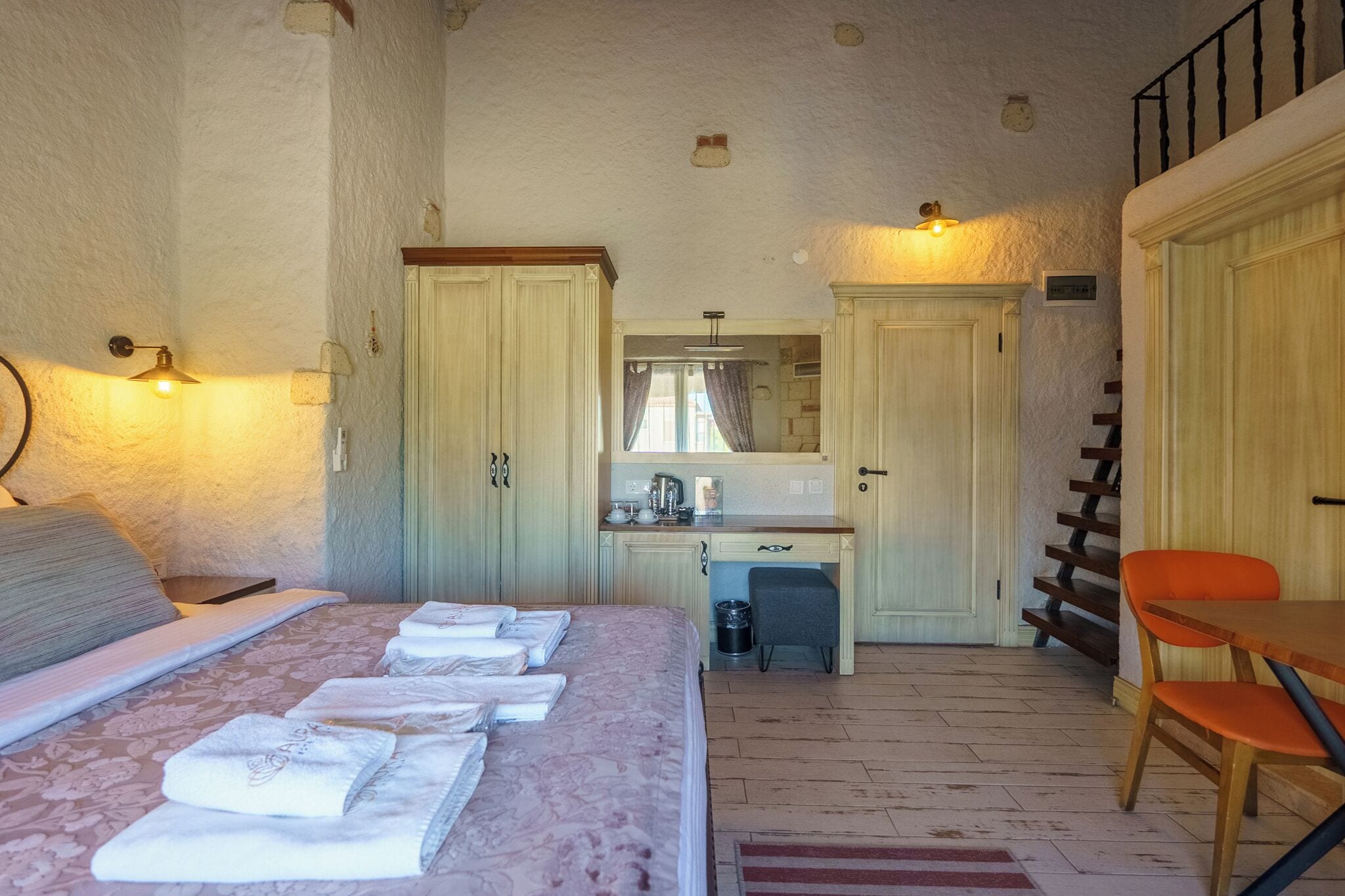 A bedroom with a bed, a desk, a chair, and a staircase.