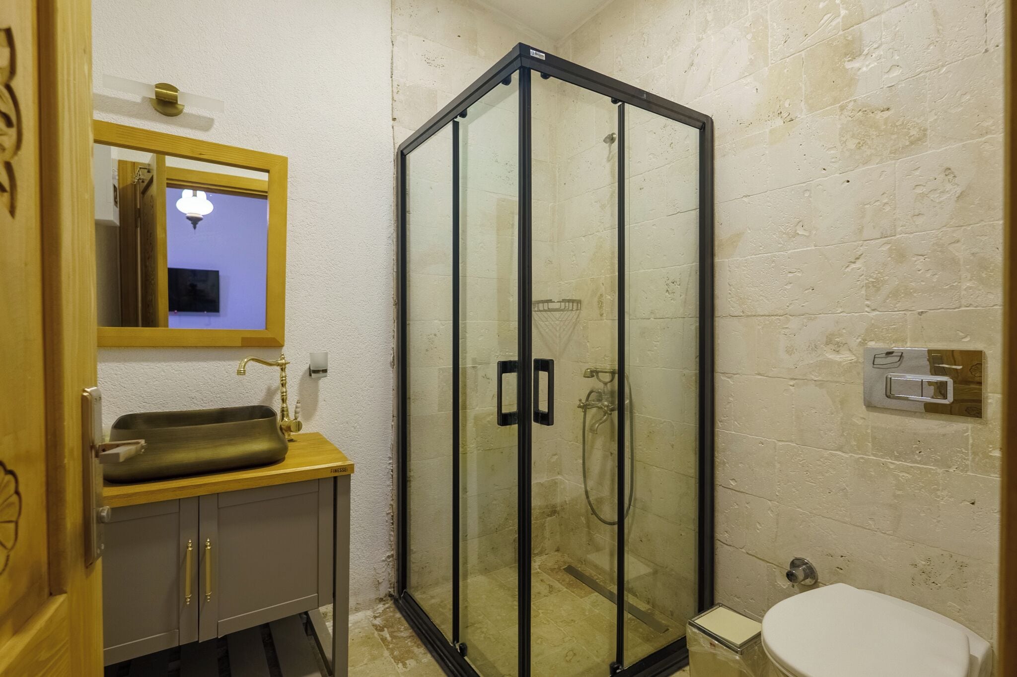 A bathroom with a glass-enclosed shower, a wooden vanity with a sink, and a toilet.