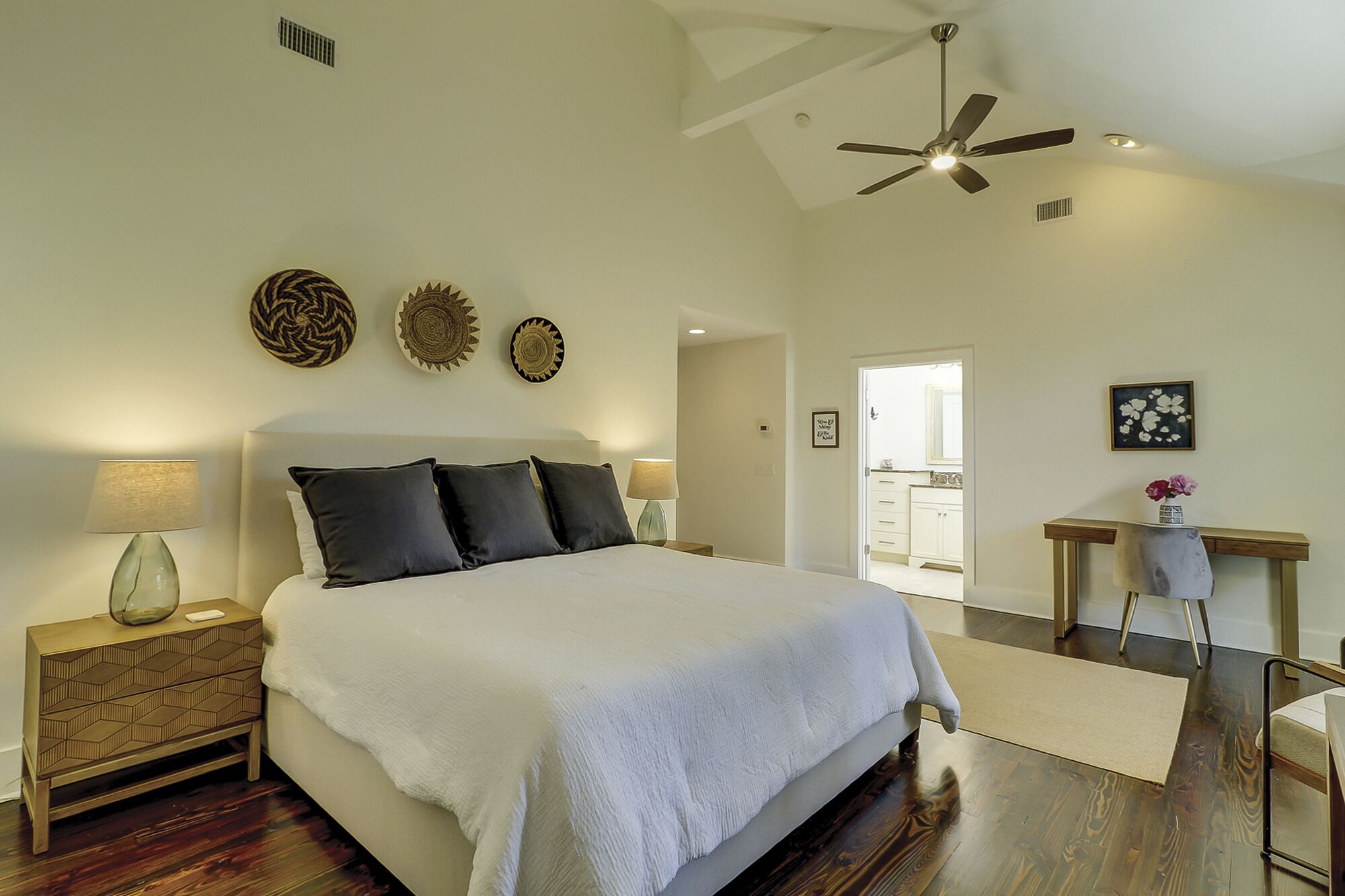 A bedroom with a large bed, a ceiling fan, and a view to the outside.