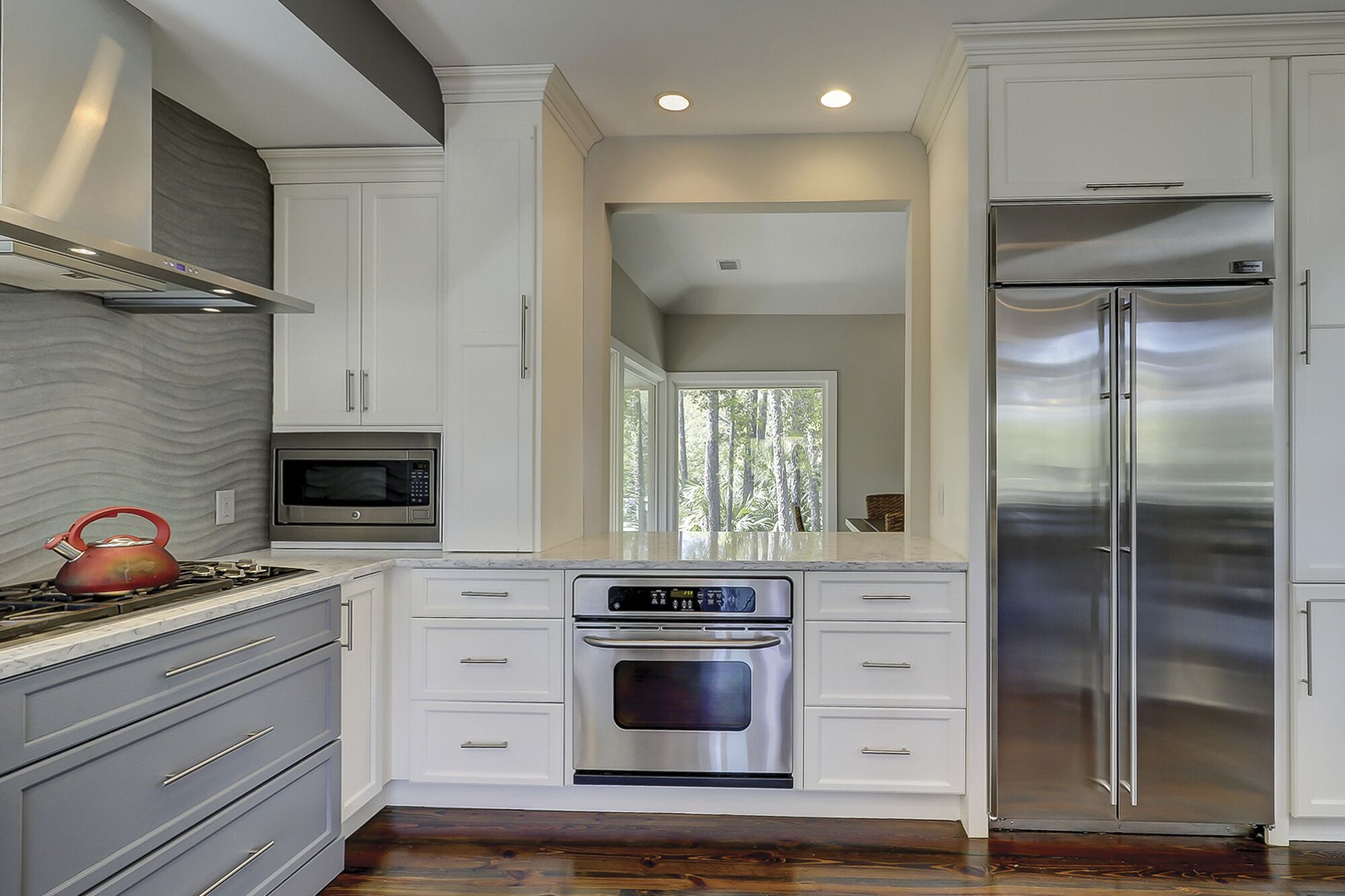 A modern kitchen with white cabinetry, stainless steel appliances, and a wooden floor.