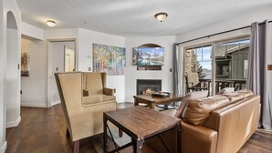 A spacious living room with a fireplace, leather sofa, and a large window offering a mountain view.
