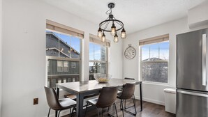 A modern kitchen with a large island, stainless steel refrigerator, and large windows offering views of a residential area.