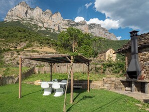 A patio with a table and chairs, a stone chimney, and a mountain backdrop. - Casa La Esencia Luxe- WIFI-BBQ-Hydromassage. Parking (San Lorien)
