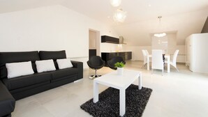 Een moderne woonkamer met een zwarte bank, een witte salontafel en een eethoek met witte stoelen.