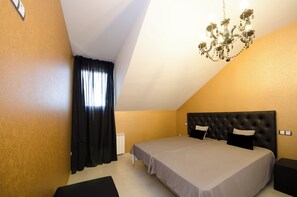 A bedroom with a large bed, a chandelier, and a window with curtains.