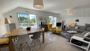 A modern living room with a wooden dining table, grey and yellow chairs, a grey sofa, and a TV.