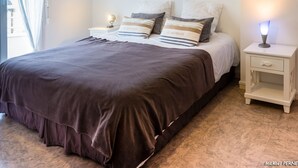 A bedroom with a large bed, two bedside tables, a nightstand, and a wall-mounted lamp.
