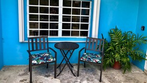 Een klein terras met twee stoelen, een tafel, een groot raam en een potplant.