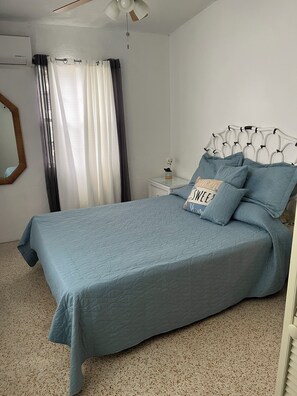 A bedroom with a bed, a nightstand, a mirror, and a ceiling fan.