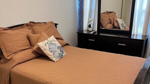 Een slaapkamer met een bed, een dressoir, een spiegel en een airconditioning.