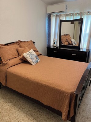 Ein Schlafzimmer mit einem Bett, einem Schminktisch, einem Spiegel und einer Klimaanlage.