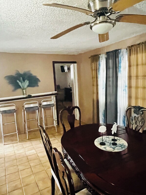 A dining area with a round table, chairs, a ceiling fan, and a view of the adjacent room. - Cozy Caribbean Home Near Beaches (Christiansted)