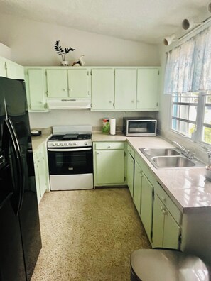 A compact kitchen with a refrigerator, stove, microwave, and sink. - Cozy Caribbean Home Near Beaches (Christiansted)
