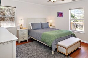 A bedroom with a bed, bedside tables, a bench, a rug, and two windows. - Blue Spring Retreat I Hot tub, Families (Wimberley)