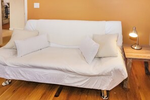 Un sofá blanco con cojines, una mesita de noche de madera con una lámpara y suelo de madera.