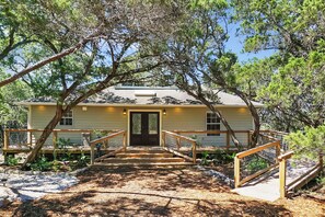 A house with a wooden deck, a front door, and a small porch area. - Blue Spring Retreat I Hot tub, Families (Wimberley)