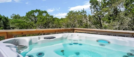 Un bain à remous doté de plusieurs jets, entouré d’une terrasse en bois et d’arbres, sous un ciel dégagé.