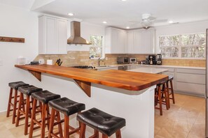 A modern kitchen with white cabinets, a wooden island with bar stools, a gas stove, and a ceiling fan.