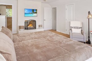 A bedroom with a large bed, a fireplace, a chair, and a television on the wall. - Blue Spring Retreat I Hot tub, Families (Wimberley)