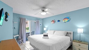 Habitación de hotel con cama, escritorio, silla, ventilador de techo y peces decorativos en la pared.