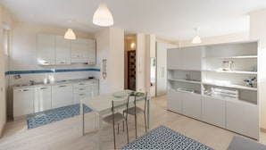 Une cuisine moderne avec des meubles blancs, une table à manger avec des chaises et des luminaires suspendus.
